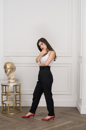 Three-quarter view of a young female looking thoughtfully at camera while standing by golden greek sculpture