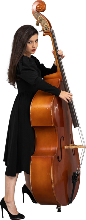 彼女のコントラバスを演奏する黒いドレスを着た真面目な若い女性ミュージシャンの側面図