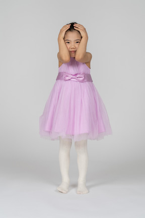 Portrait d'une petite fille en robe lavande se tenant la tête