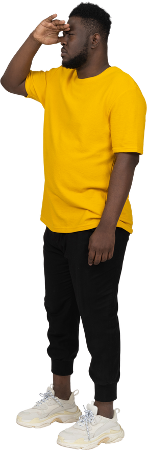 무언가를 찾고 있는 노란색 티셔츠를 입은 검은 피부의 젊은 남자의 4분의 3 보기