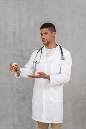 Young male doctor pointing at bottle of pills