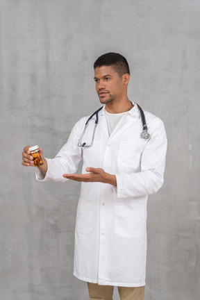 Joven médico apuntando al frasco de pastillas