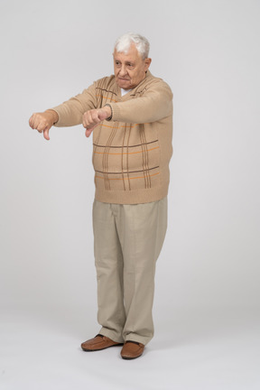 Vue de face d'un vieil homme en vêtements décontractés montrant les pouces vers le bas