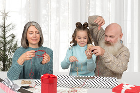 An old man and an old woman wrapping christmas gifts together with a little girl