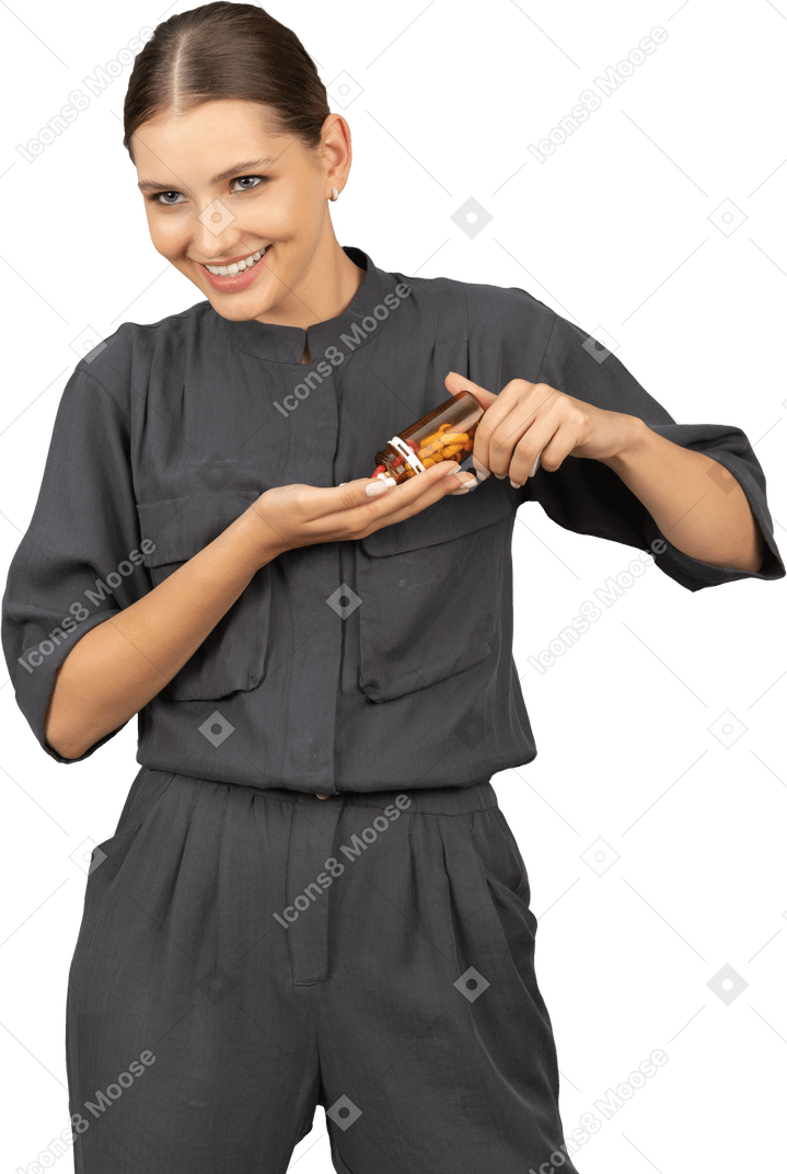 Front view of a smiling young woman in a jumpsuit pouring the pills out of a jar