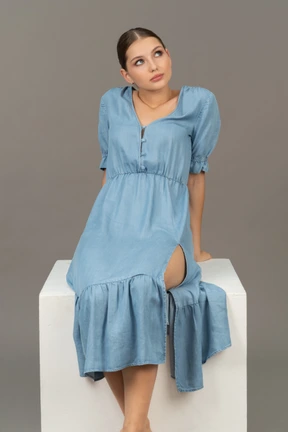 Front view of young woman sitting on a cube and looking up