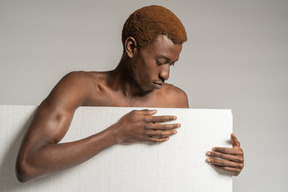 Вид спереди молодого афро-человека, стоящего за пенополистиролом и смотрящего вниз