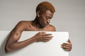 Front view of a young afro man standing behind styrofoam and looking down