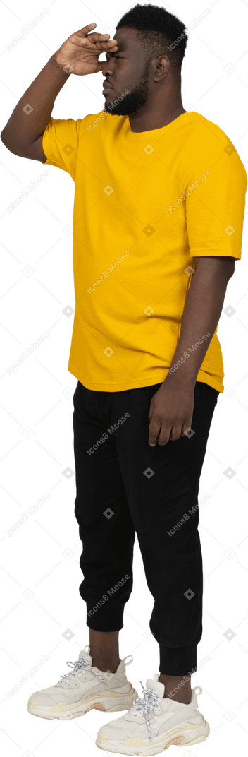 何かを探している黄色のtシャツを着た若い浅黒い肌の男の4分の3のビュー