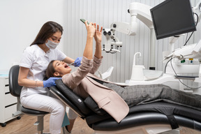 A figura intera di un dentista femminile che esamina il suo paziente che fa selfie