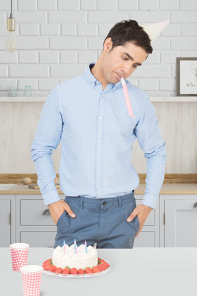 Sad man in party hat standing in front of a cake with candles on it