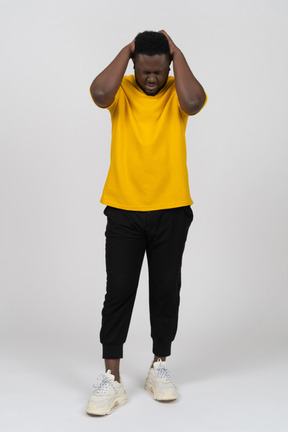 Front view of a young dark-skinned man in yellow t-shirt touching head