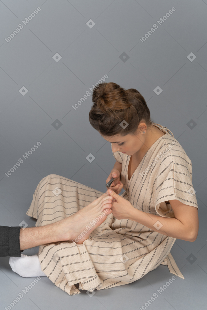 一个年轻的女人，帮助一个男人安排他的脚趾甲