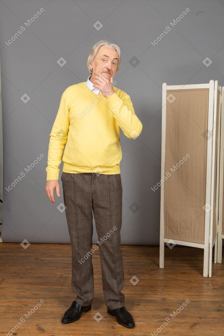 Front view of a thoughtful old man touching chin while looking at camera