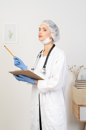 Трехчетвертный вид молодой женщины-врача, держащей карандаш и планшет