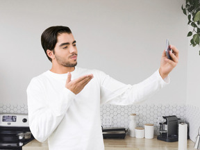 A man blowing a kiss while taking selfie on smartphone