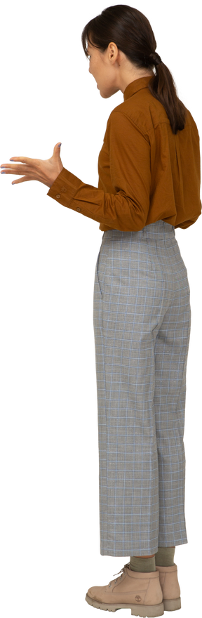 Вид сзади в три четверти молодой жестикулирующей азиатской женщины в бриджах и блузке