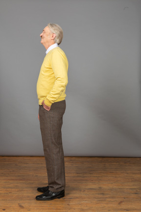 Vue latérale d'un vieil homme heureux portant un pull jaune et mettant la main dans la poche