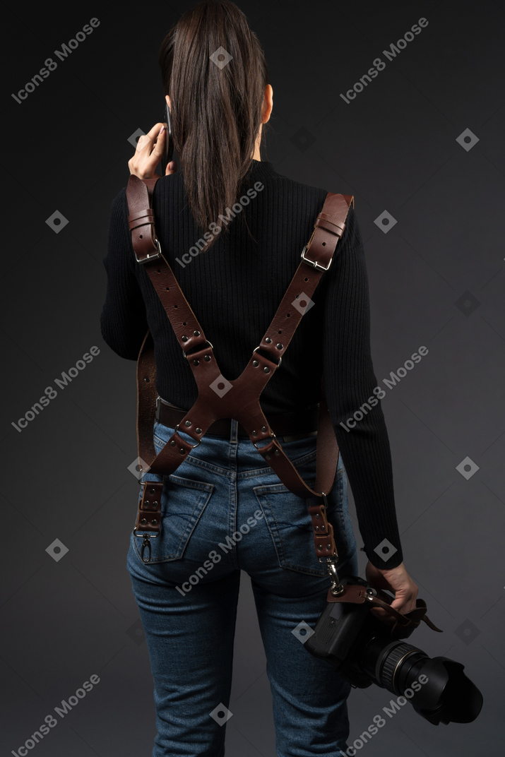Female photographer standing backwards to camera while talking by phone
