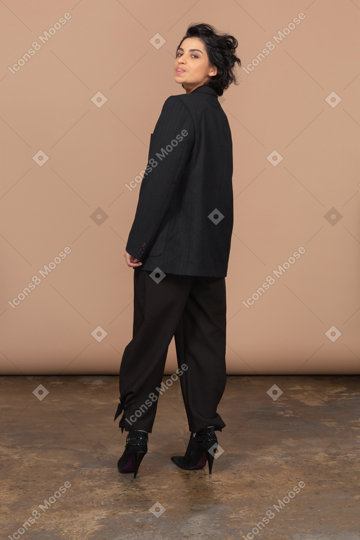 Vista traseira de uma mulher de negócios em um terno preto, mostrando a língua e olhando para a câmera