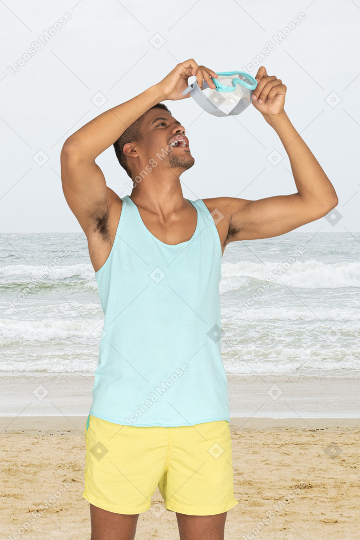 A man standing on a beach holding goggles
