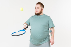 Tipo grande en ropa deportiva recogiendo pelota de tenis con raqueta de tenis