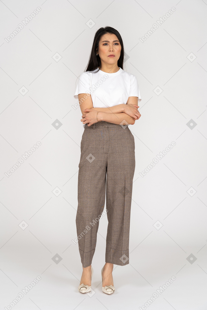 Vista frontale di una giovane donna sospettosa in calzoni e t-shirt attraversando le mani