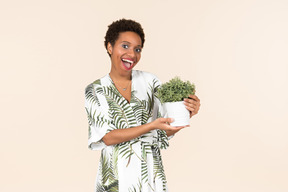 Young black short haired woman in a dressing gown, holding a potted plant