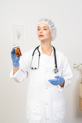 Front view of a young female doctor holding a jar of pills