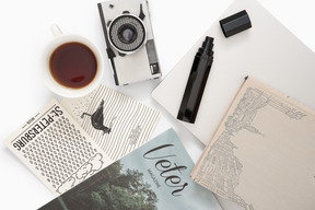 Desk with closed laptop, pile of magazines, photocamera and cup of tea