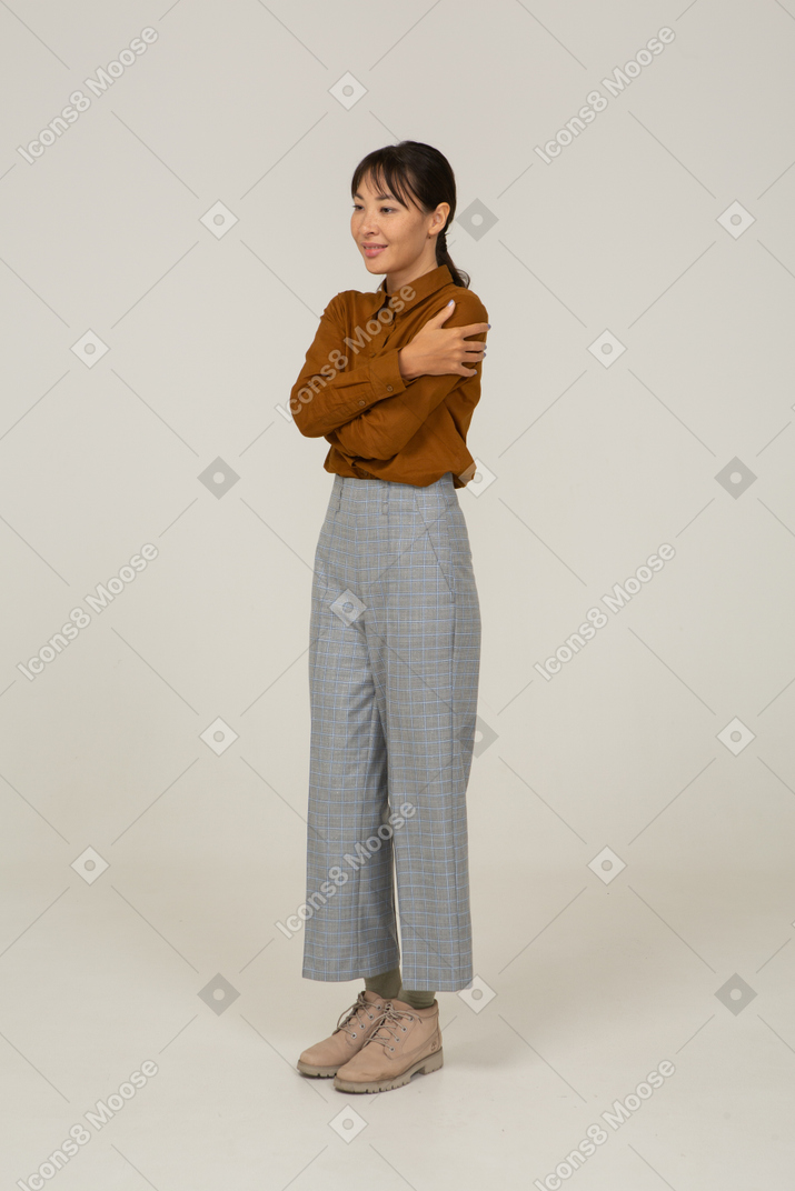 一位身着马裤和衬衫的年轻亚洲女性拥抱自己的四分之三视图