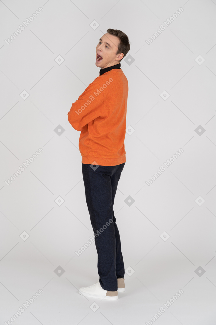 Junger mann im orangefarbenen pullover, der mit gekreuzten armen steht