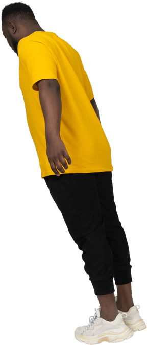 Three-quarter back view of a young dark-skinned man in yellow t-shirt leaning forward & outstretching arm