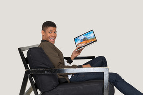 Vista laterale del giovane seduto su un divano e con in mano un laptop