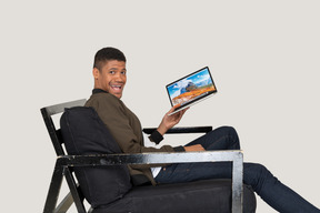 Side view of young man sitting on a sofa and holding a laptop