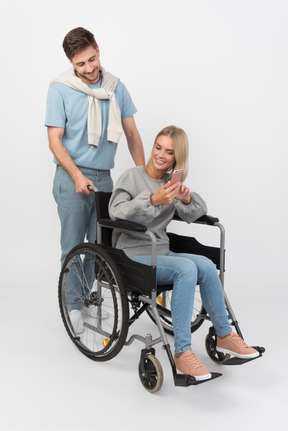 Guy driving a wheelcahir and disabled girl showing him something on the phone