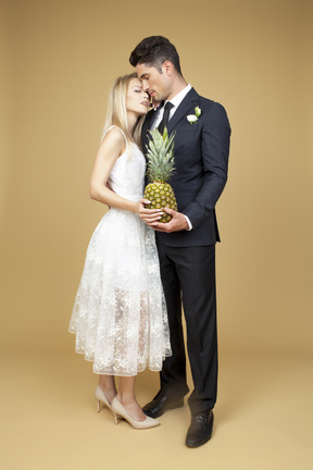 Bride and groom standing shoulder to shoulder and holding a pineapple