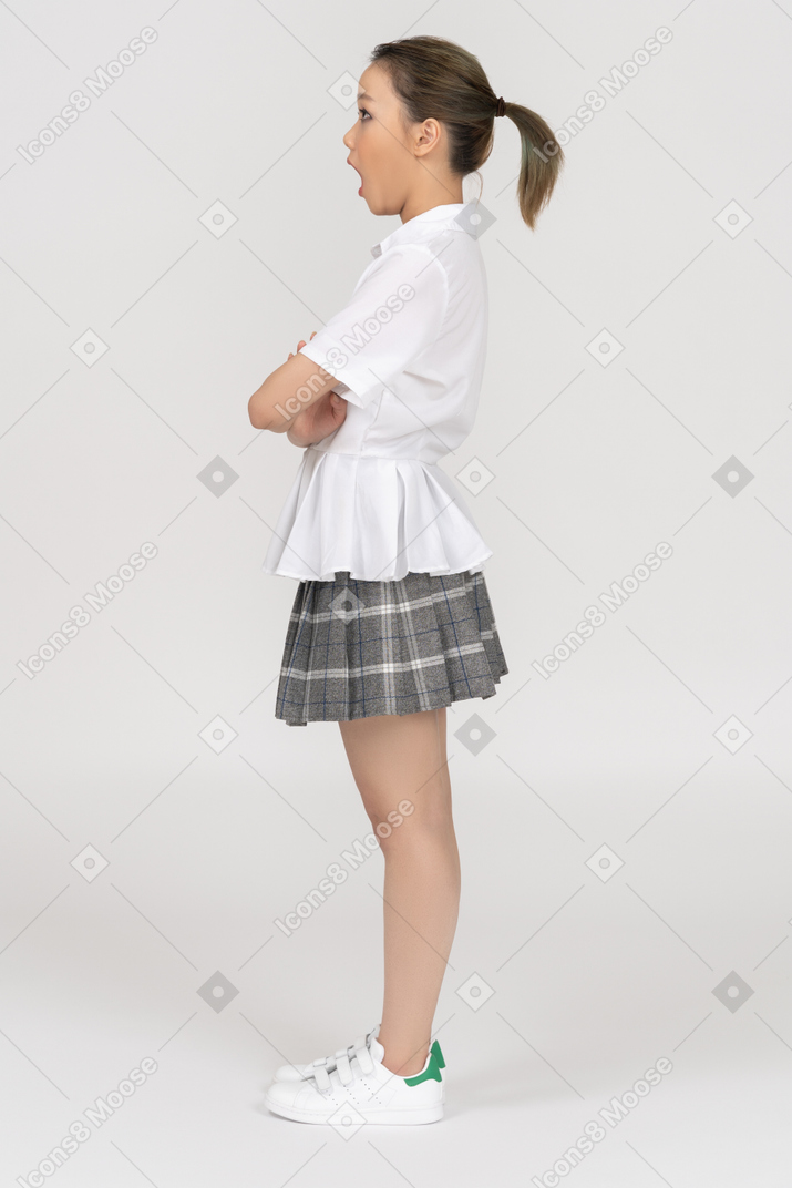 Uma menina asiática surpresa, de pé lateralmente para uma câmera