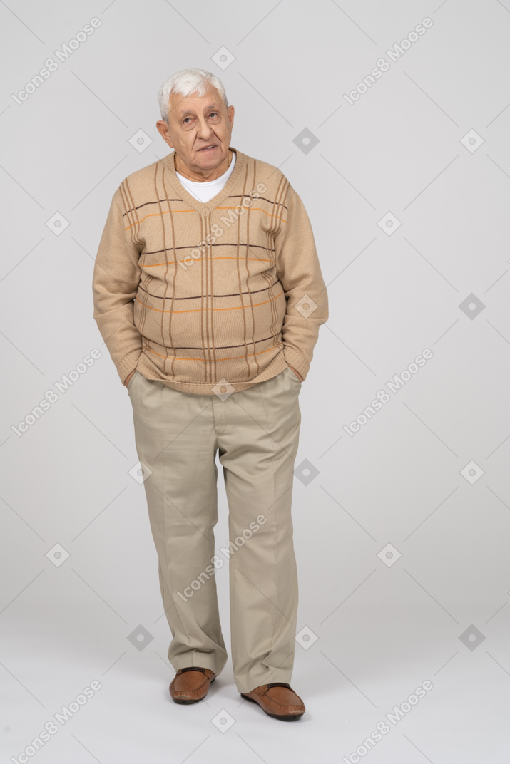 Front view of an old man in casual clothes standing with hands in pockets