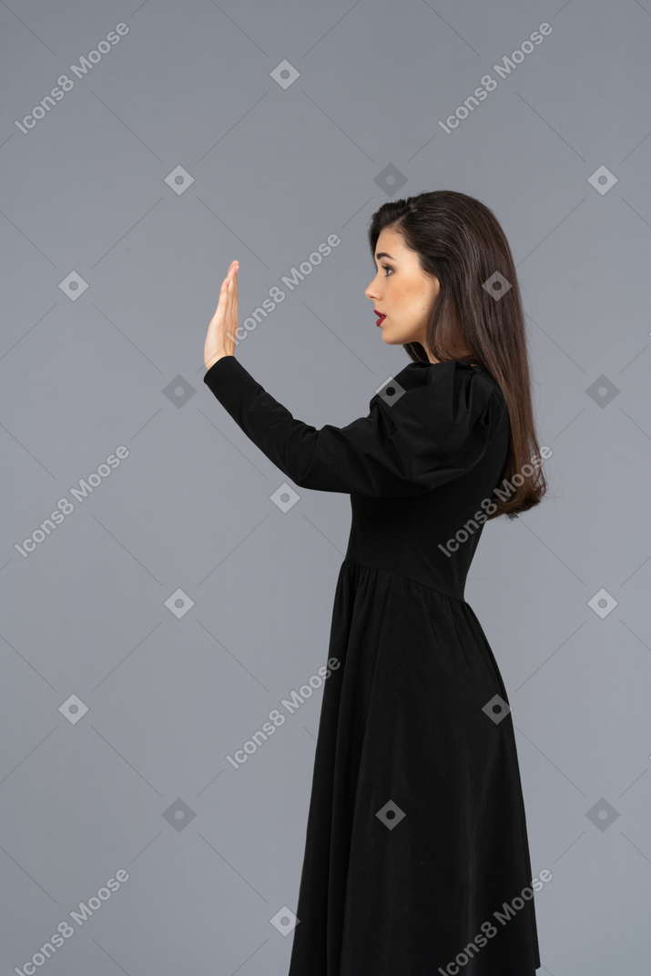 一位年轻的女士，穿着黑裙子举起她的手的侧视图