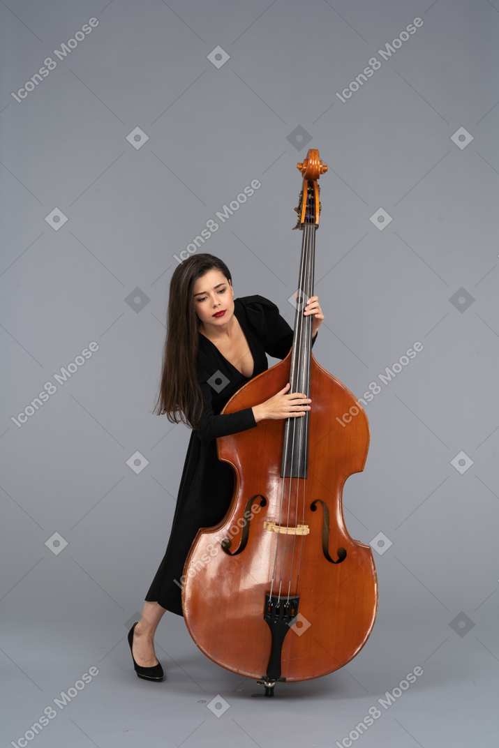Vista frontale di una giovane donna in abito nero che suona il contrabbasso e guarda in basso