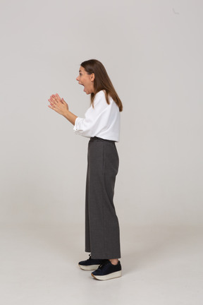 Vista lateral de uma jovem animada com roupa de escritório, levantando as mãos