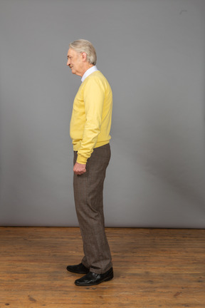 Side view of a depressed old man wearing a yellow pullover and looking aside