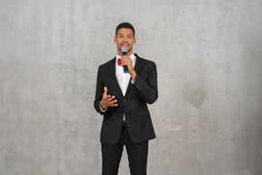Hombre sonriente con traje negro hablando al micrófono