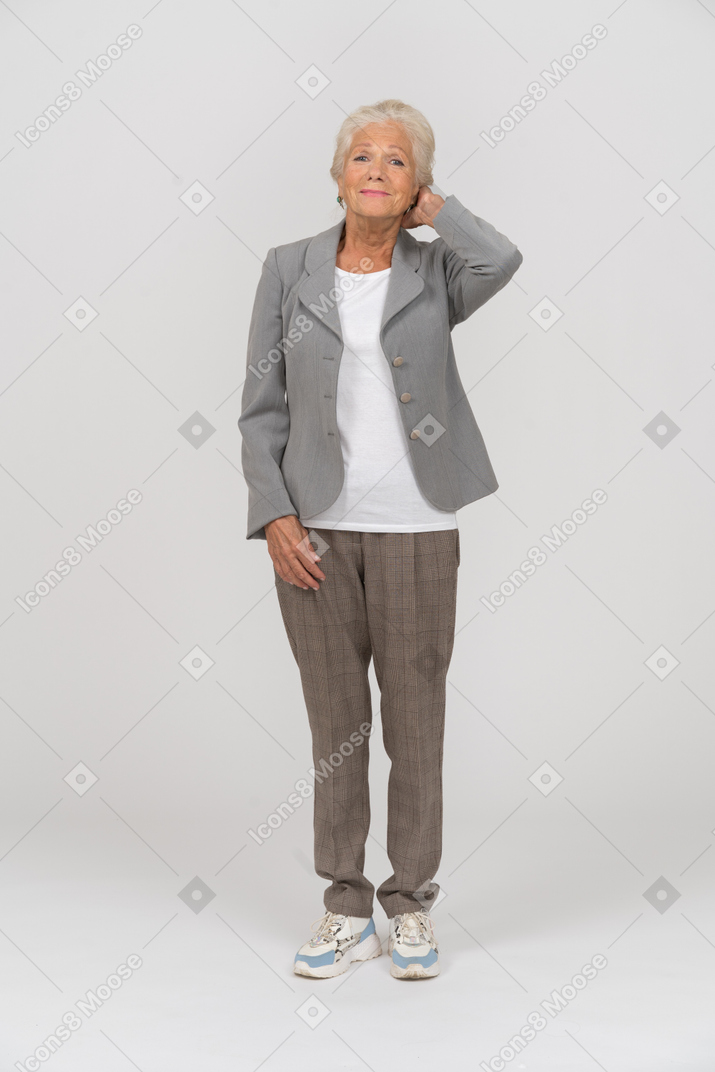 Front view of an old lady in suit standing with hand behind head