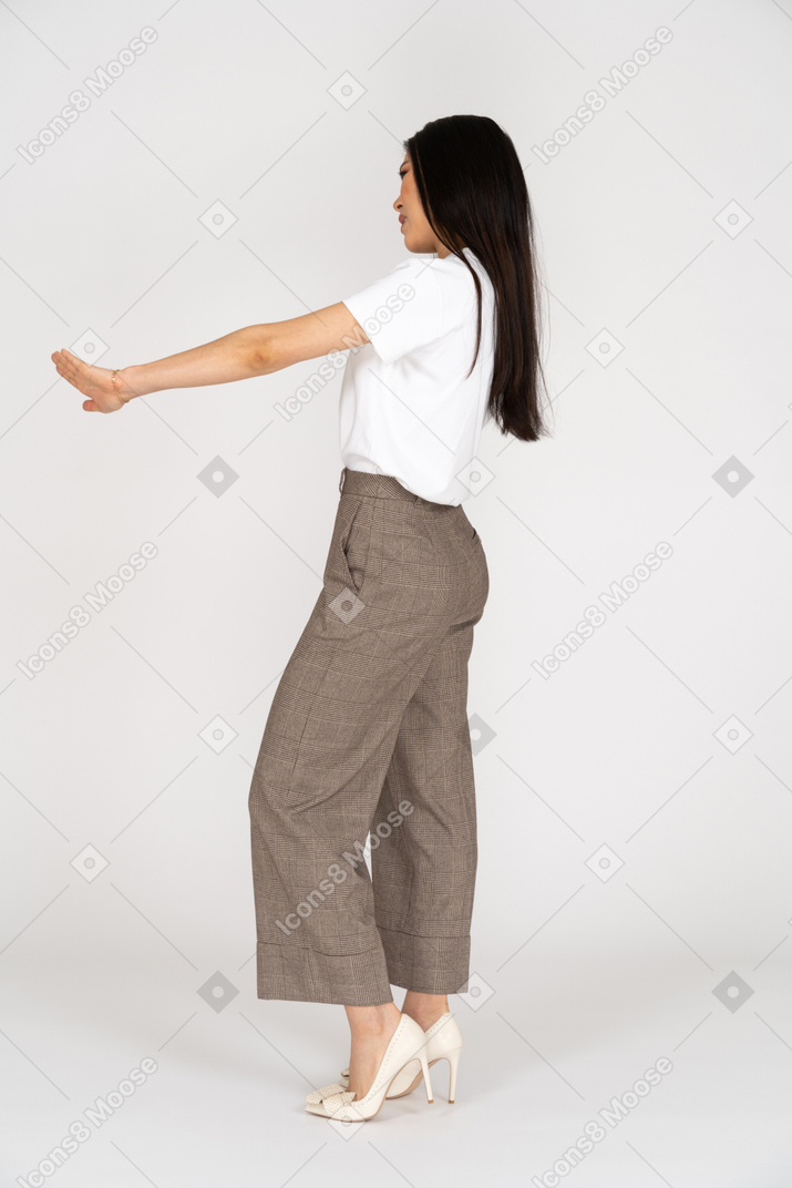 Vista lateral de uma jovem de calça esticando a mão