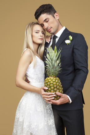 Bride and groom standing shoulder to shoulder and holding a pineapple