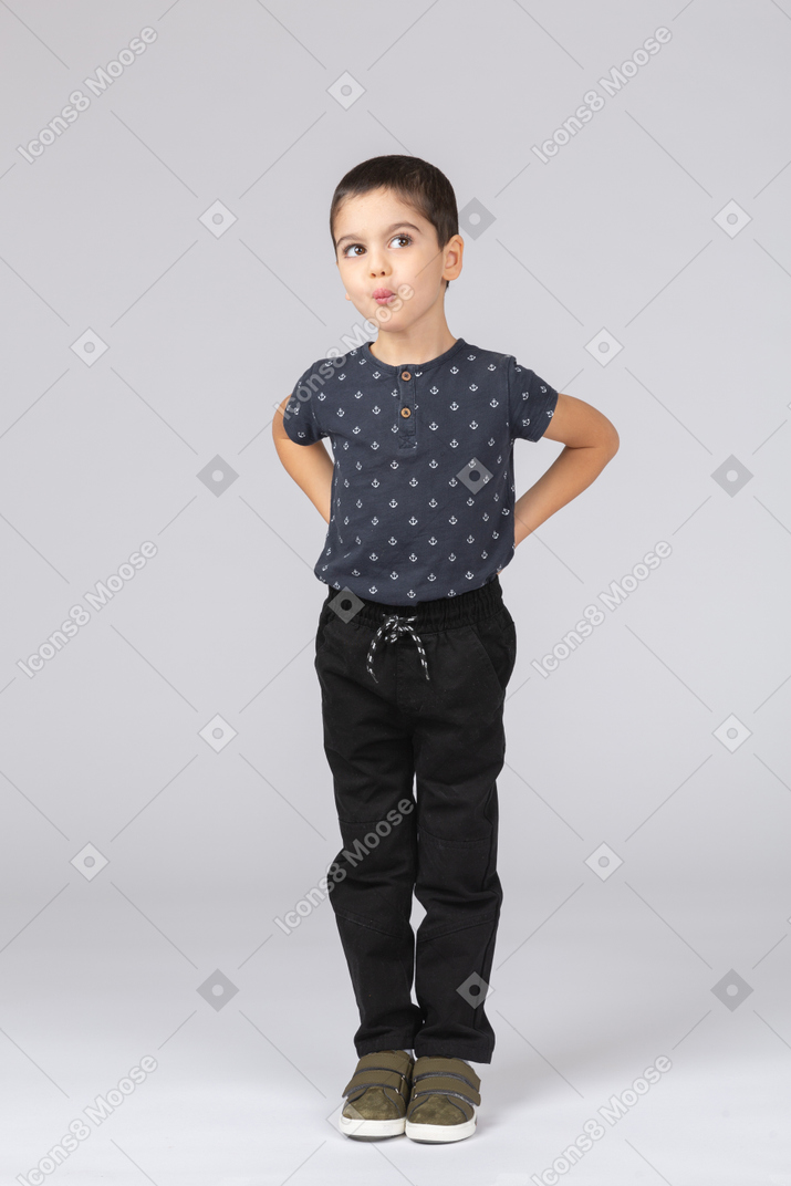 Vista frontale di un ragazzo carino in abiti casual in posa con le mani dietro la schiena
