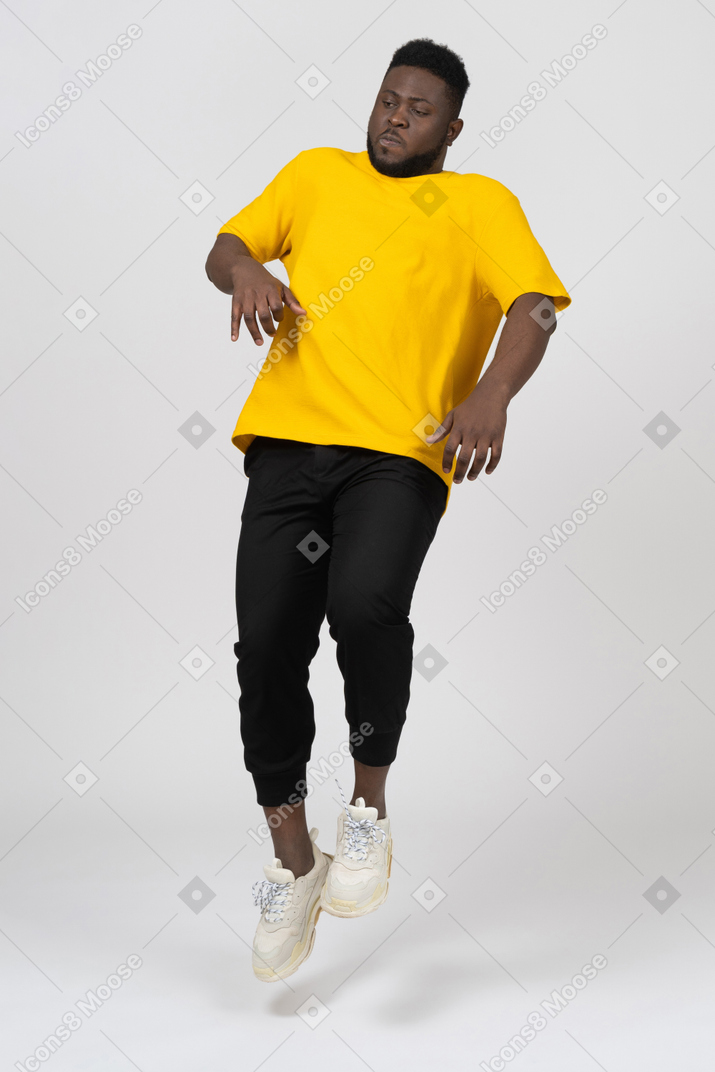 Front view of a young dark-skinned man in yellow t-shirt jumping back