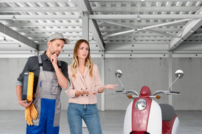 A man and a woman standing next to a scooter